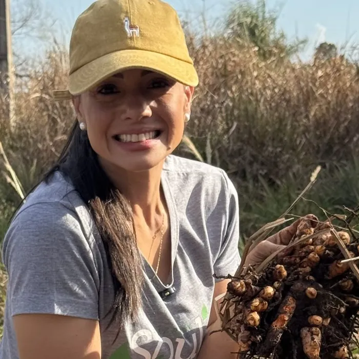 Juliana Trombini sorrindo na lavoura, segurando raízes de cúrcuma recém-colhidas