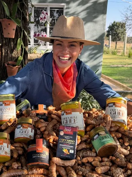 Juliana com produtos da Fazenda Soul Leve sobre um monte de cúrcuma colhida